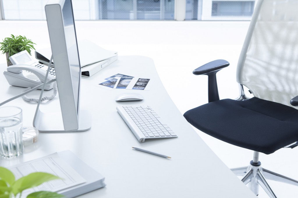 clean white commercial office desk with desktop computer phone books and chair